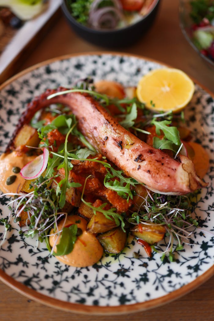 Delicious grilled octopus served with roasted vegetables and microgreens on a patterned plate.